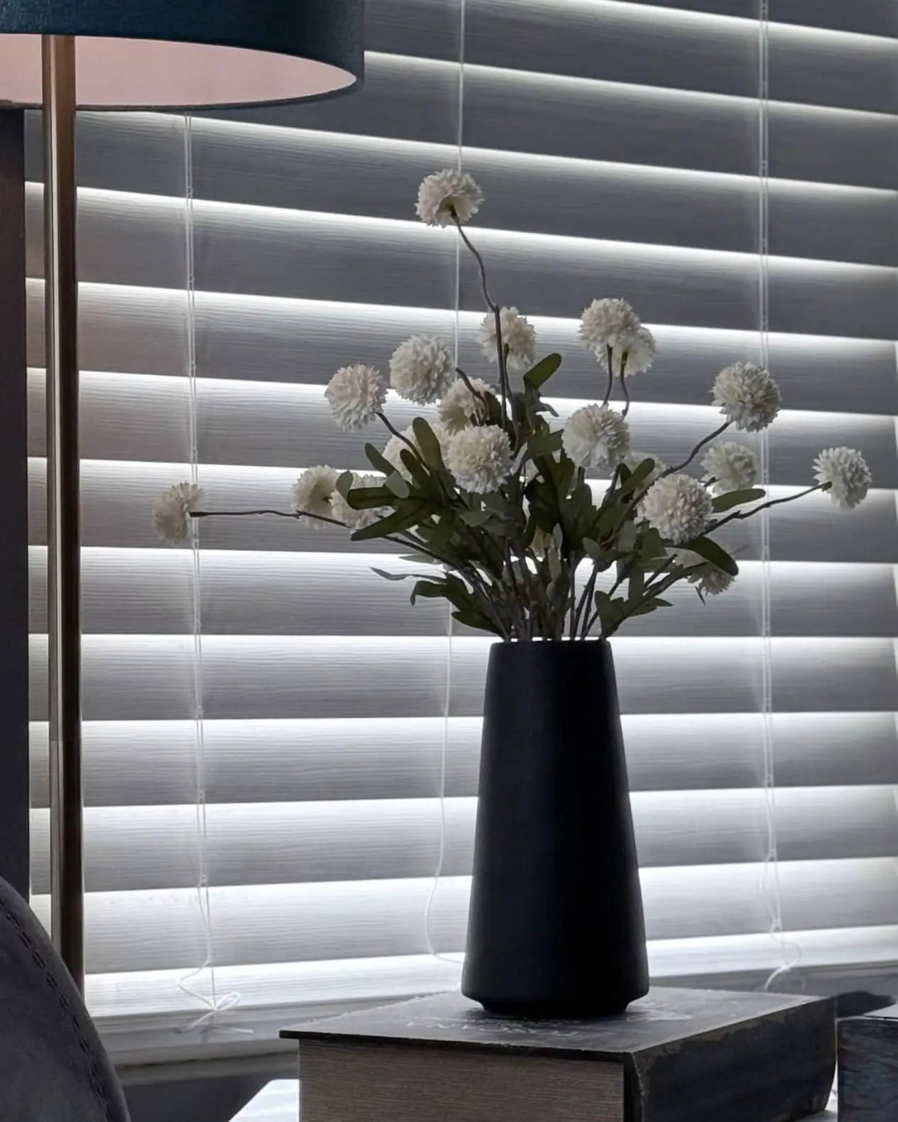 White pompon mums in a black vase beside a window