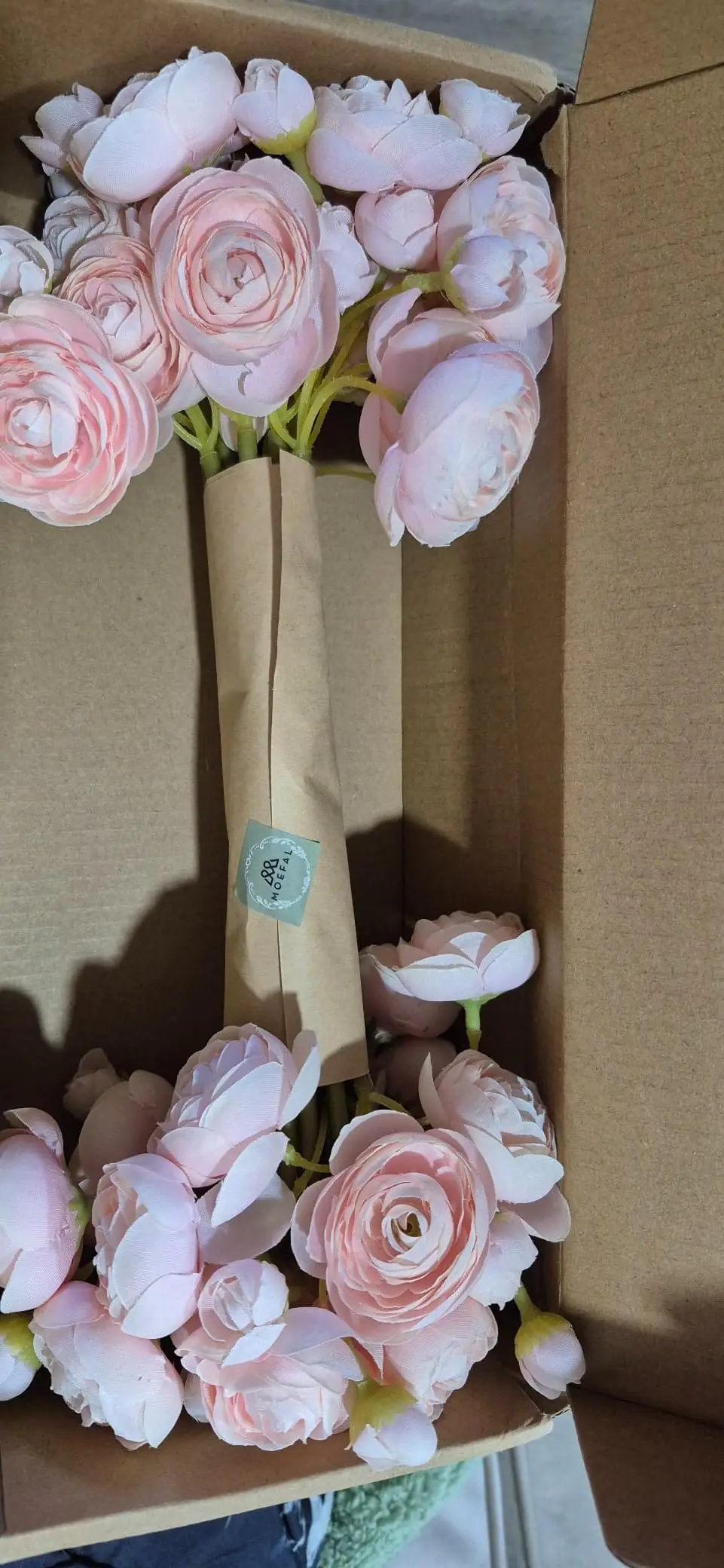 Blush pink ranunculus stems packed in the shipping box with the paper sleeve