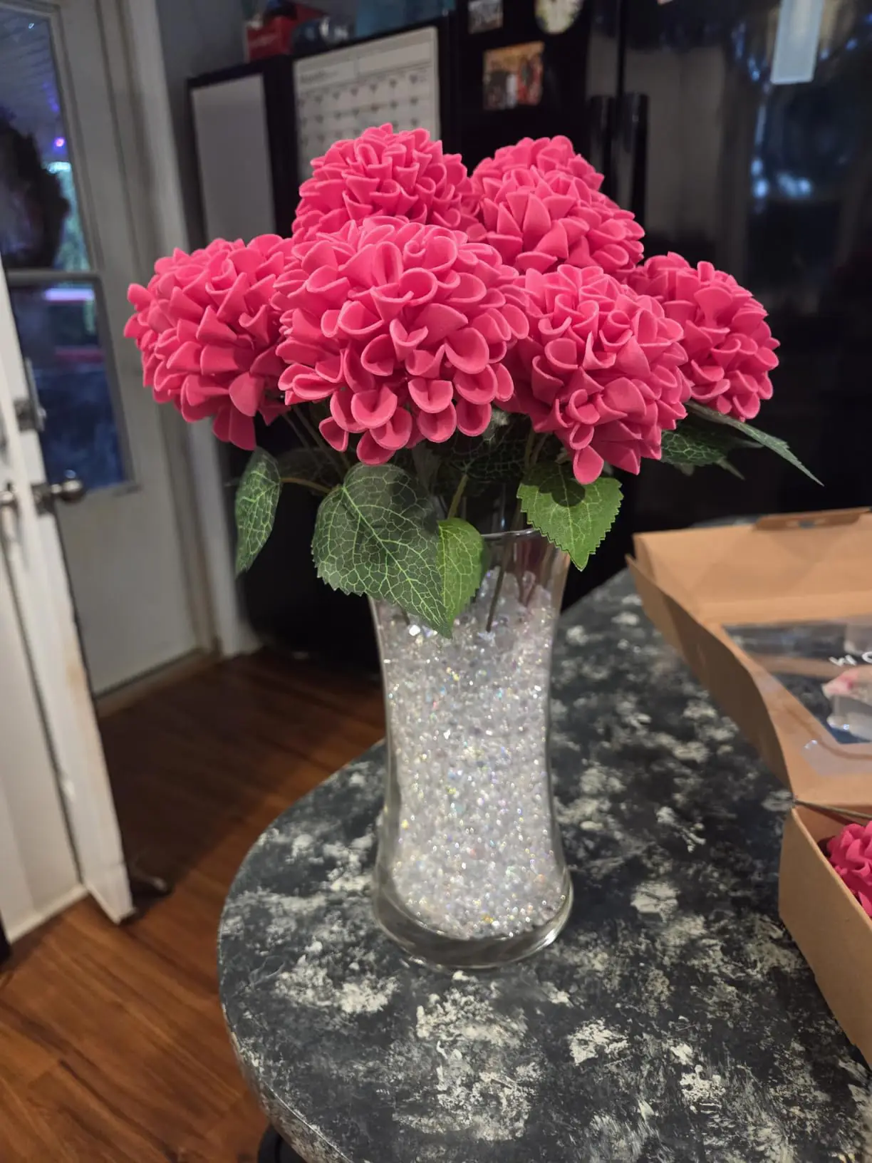 Hot pink foam dahlias with green leaves arranged in a tall glass vase