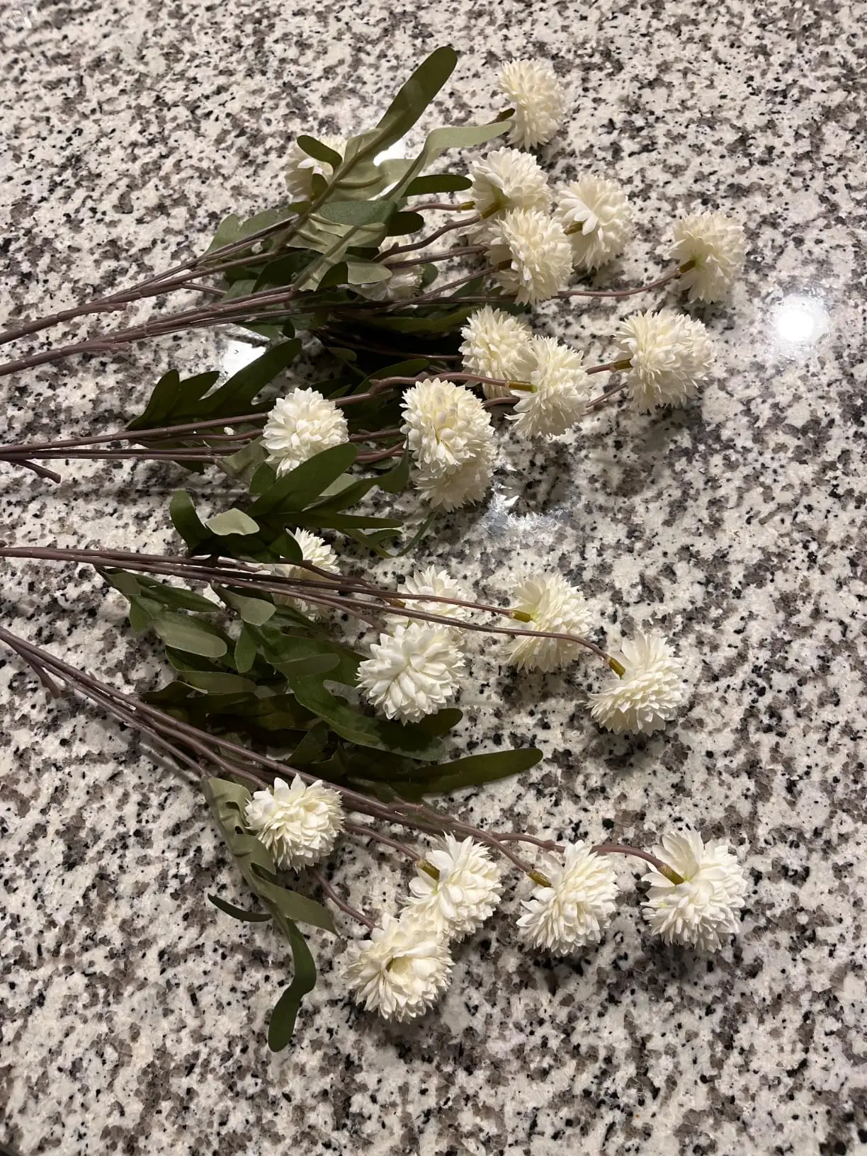 White pompon mum stems laid out on a granite counter