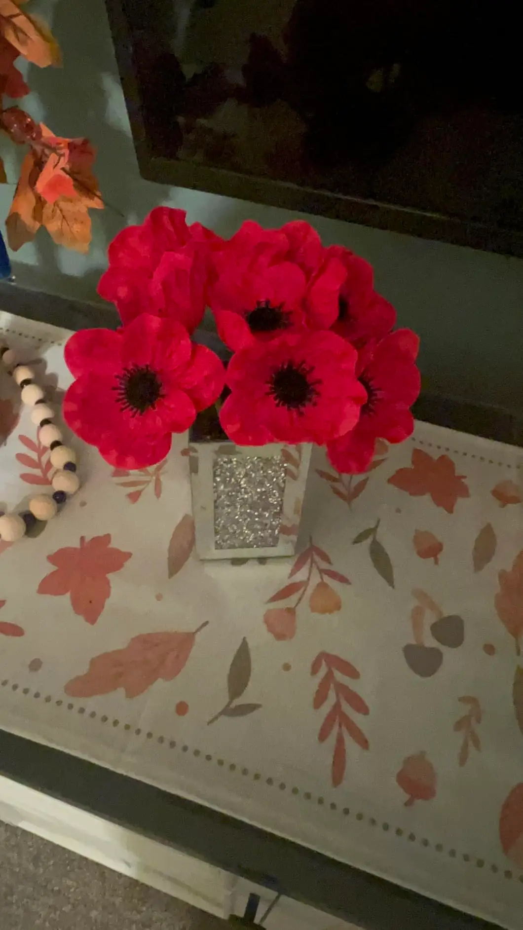 Red anemone poppies in a glitter cube vase on an autumn table runner