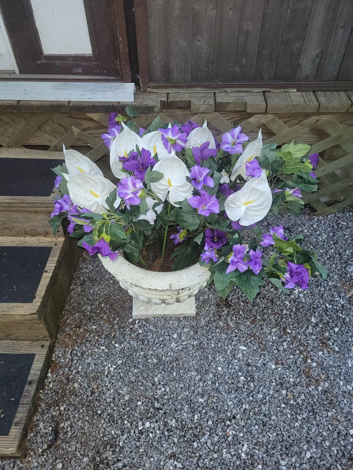 White artificial anthuriums arranged with purple flowers in a stone urn
