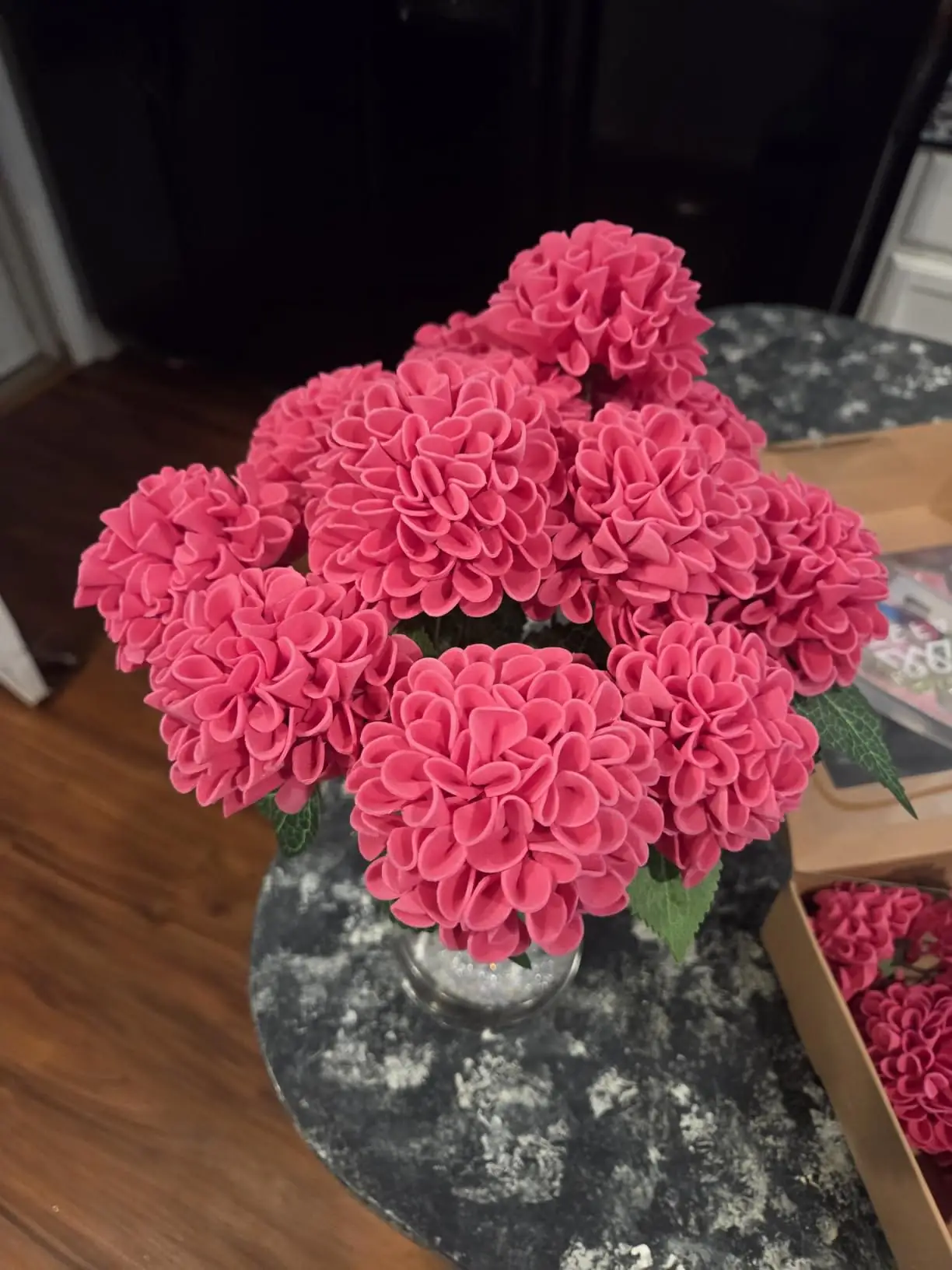 Hot pink foam dahlias gathered in a glass vase on a kitchen table