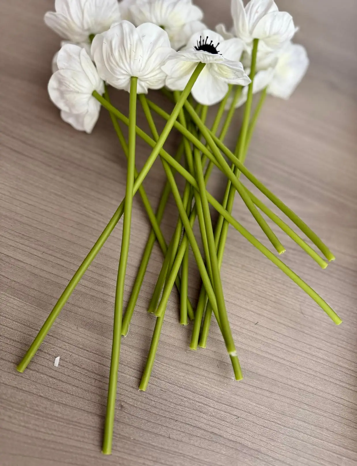 White anemone poppies laid on a wood table with long green stems
