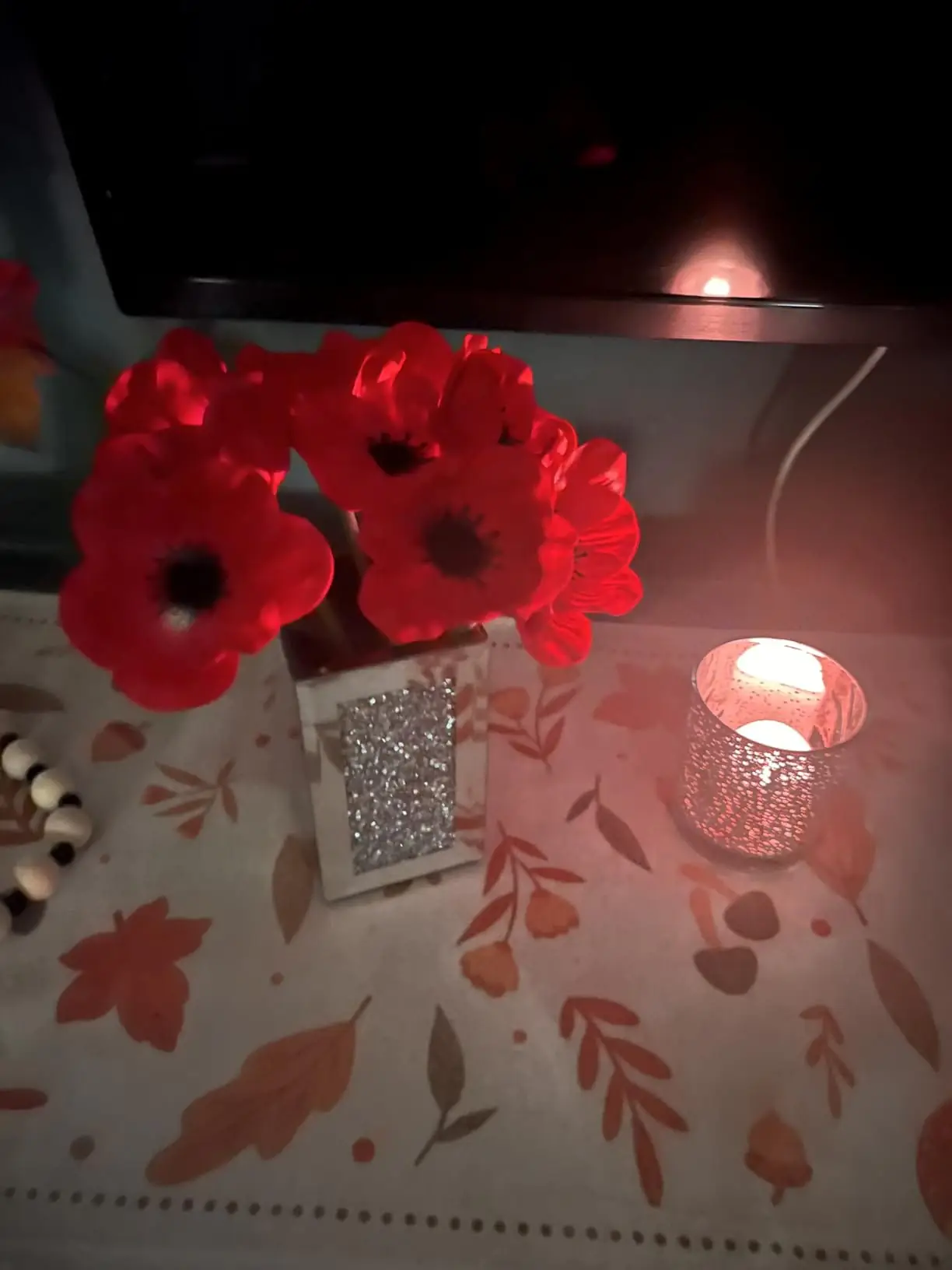 Red anemone poppies in a glitter vase beside a lit candle