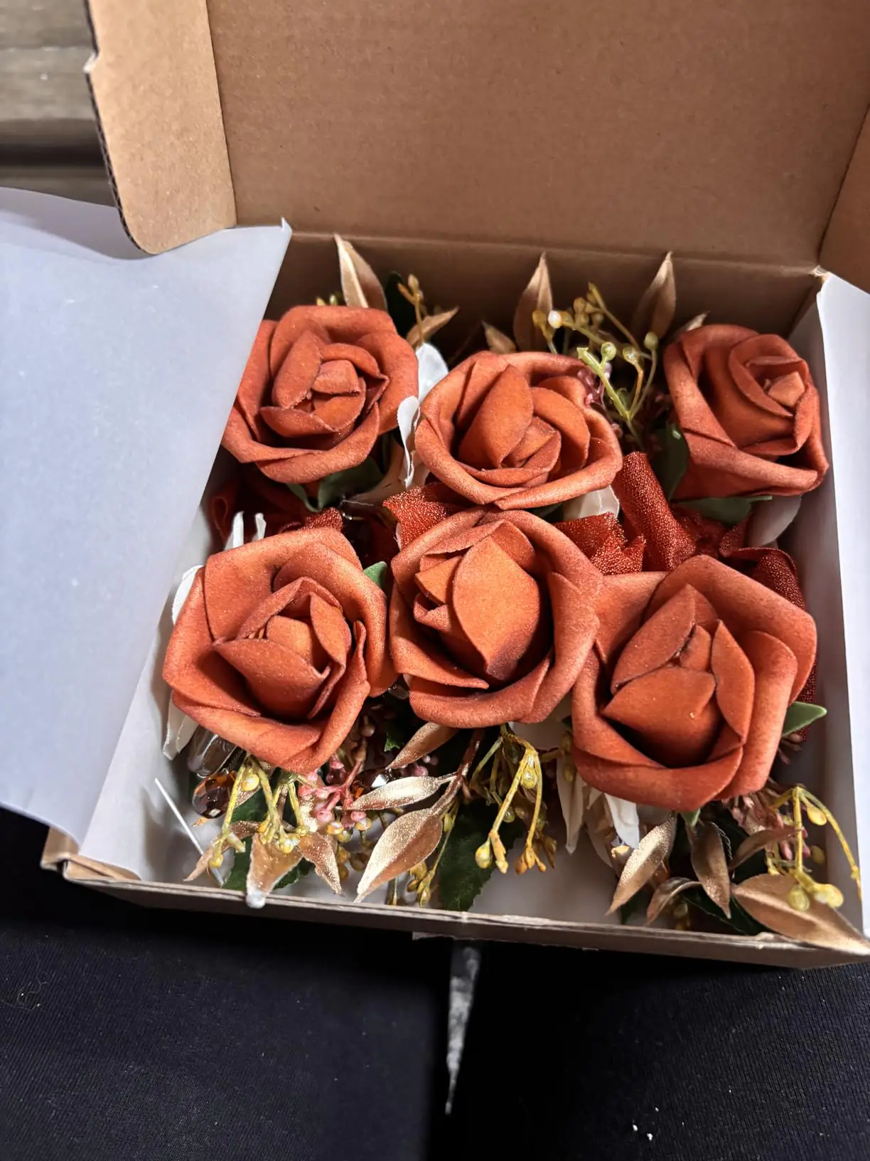 Six terracotta rose boutonnieres neatly boxed with greenery and gold accents