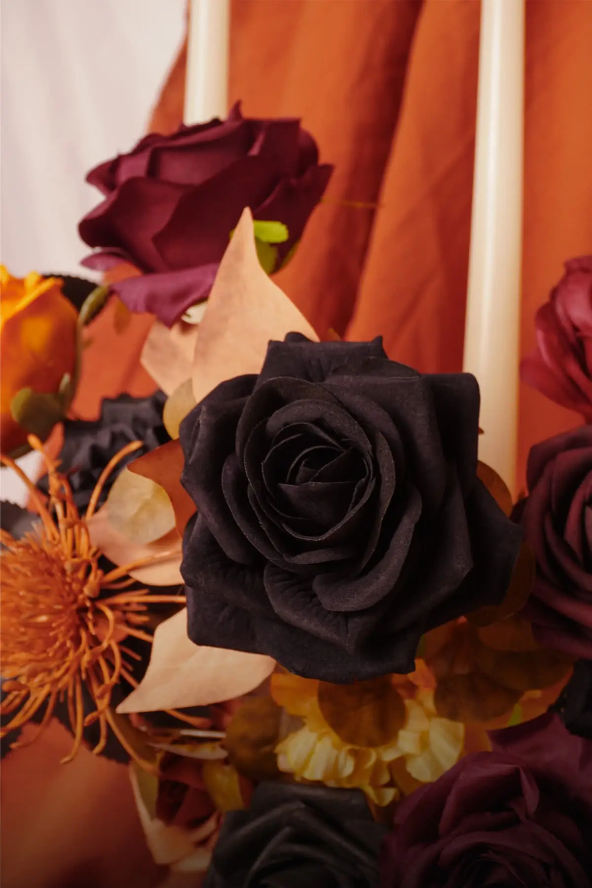 Close-up of a black artificial rose with layered silk petals beside wine red roses and blush-orange leaves from the MOEFAL Halloween flower box
