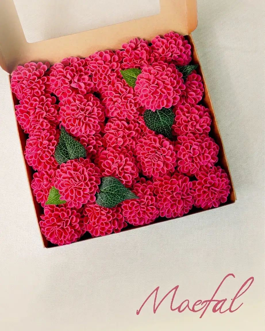 Top-down view of many hot pink artificial dahlia flower heads packed in a box.