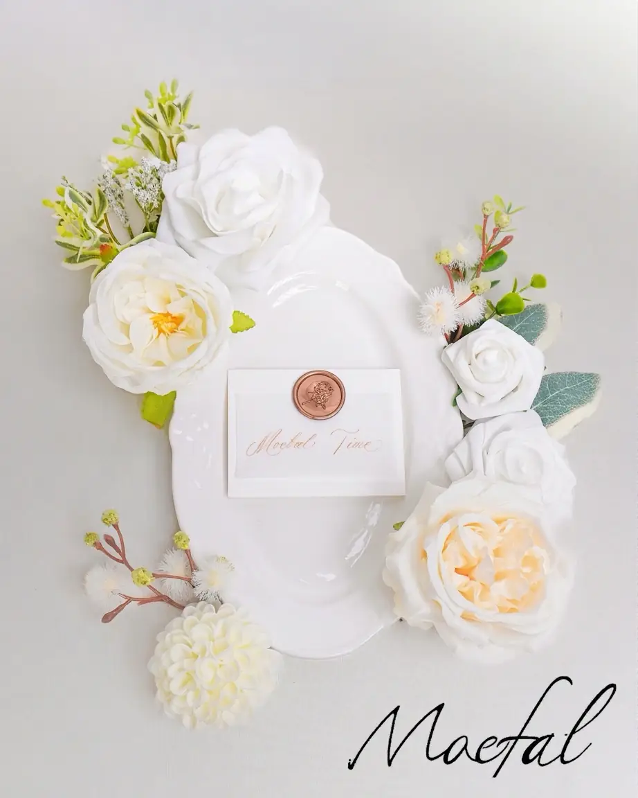 A classic white plate and card surrounded by loose ivory wedding flowers for a table setting.