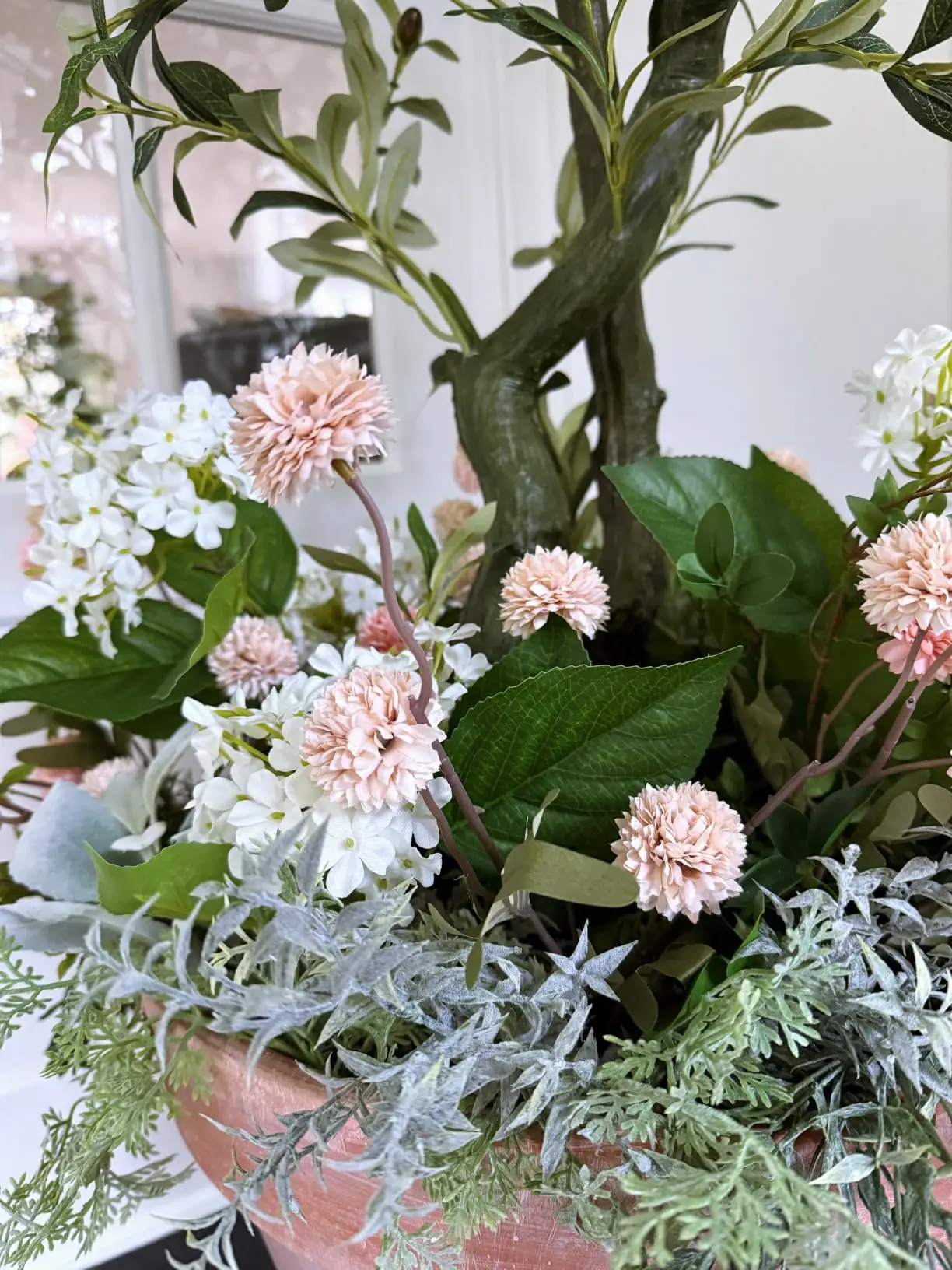 Beige pompon mums arranged with white and pink blooms in a terracotta pot